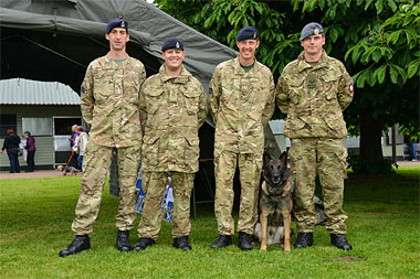 4 smiling soliders standing in a row with an alsation dog