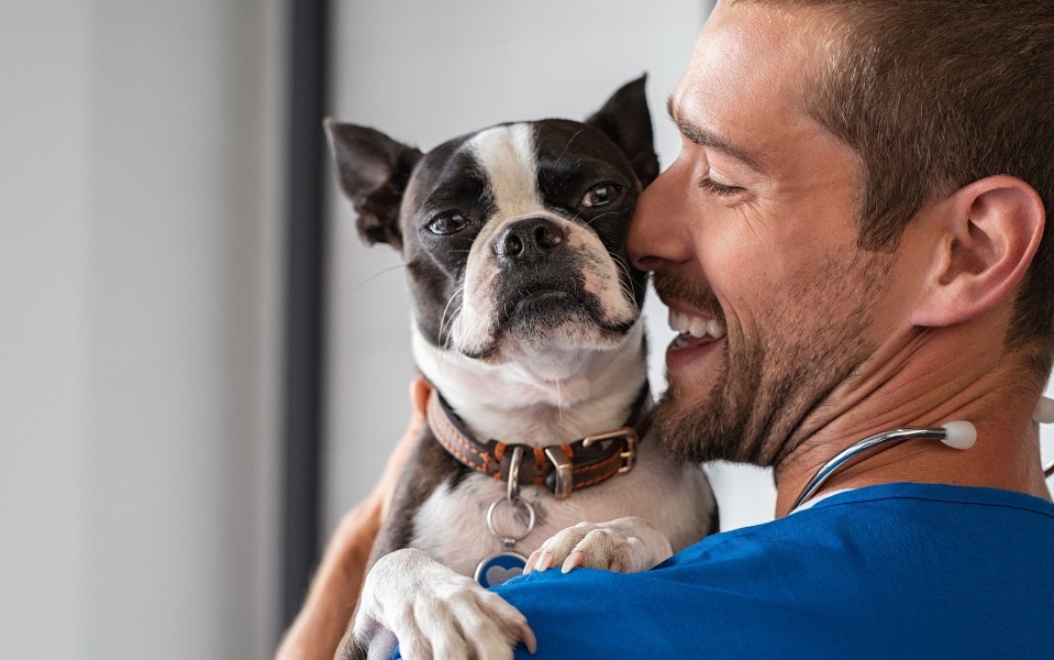 Vet smiling and holding up a dog on his shoulder
