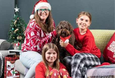 Family sitting on the couch in Christmas jumpers with their dog