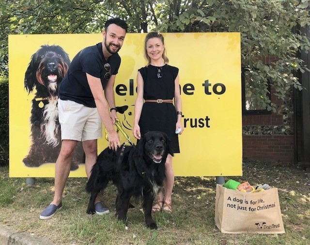 Man and woman standing in front of large yellow Dogs Trust banner holding Bobby on a leash