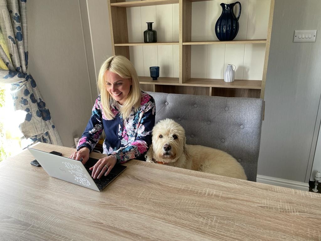 Sarah sitting at a desk typing on a laptop with dog